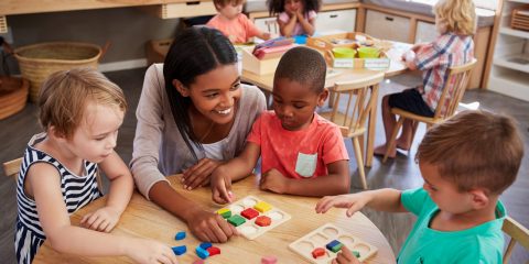 Teacher And Pupils Using Wooden Shapes In Montessori School